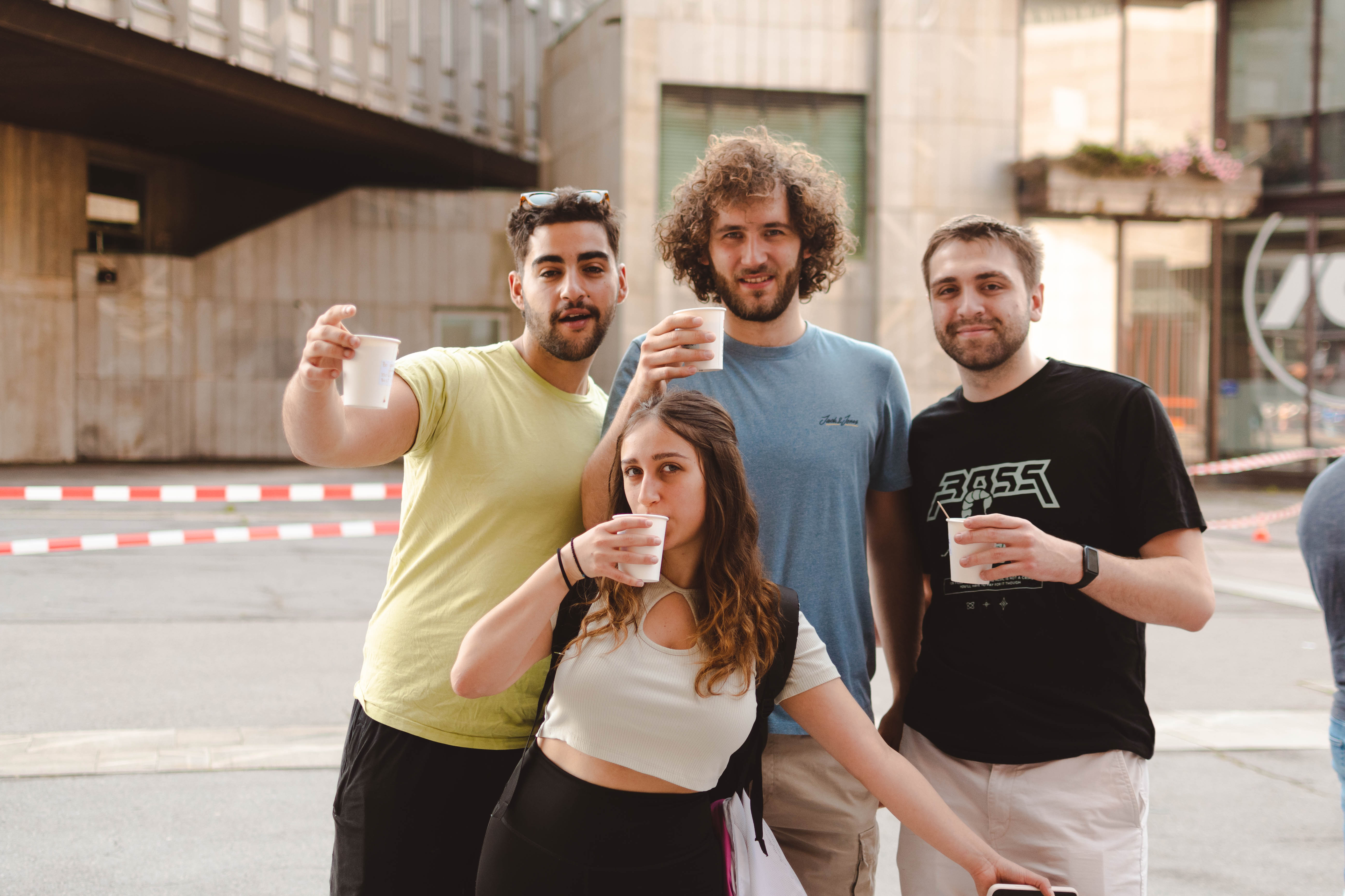 Skupina študentov s toplo kavo pozira pred kamero.