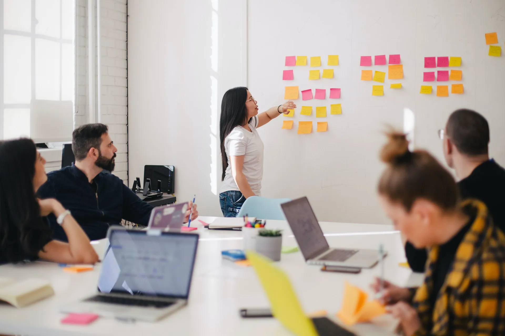 A woman presenting in front of a whiteboard with sticky notes to a team