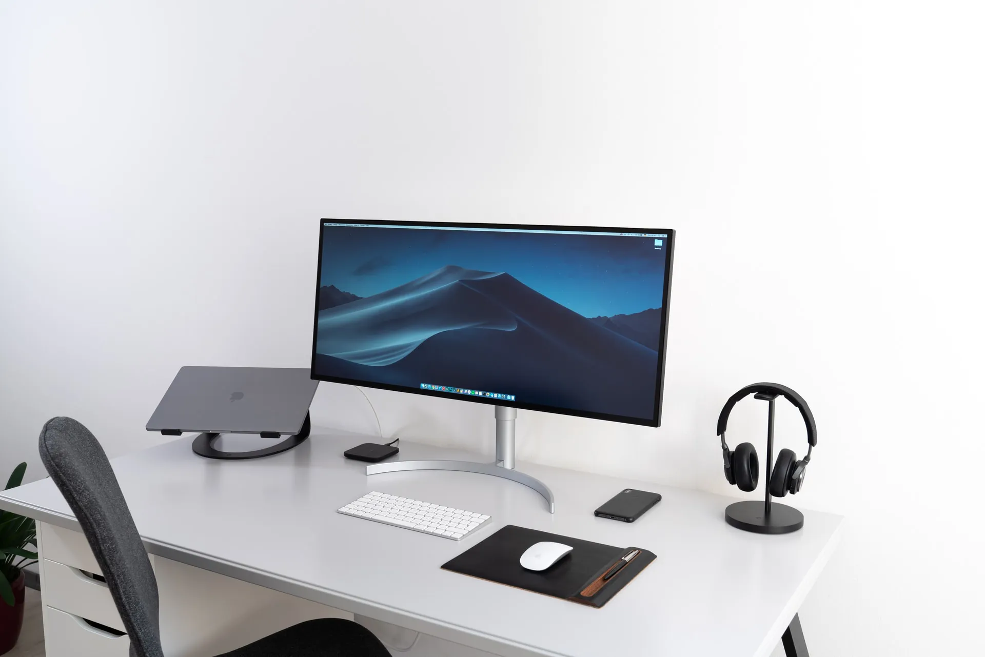 A modern computer desk setup with a large monitor, keyboard, and headphones